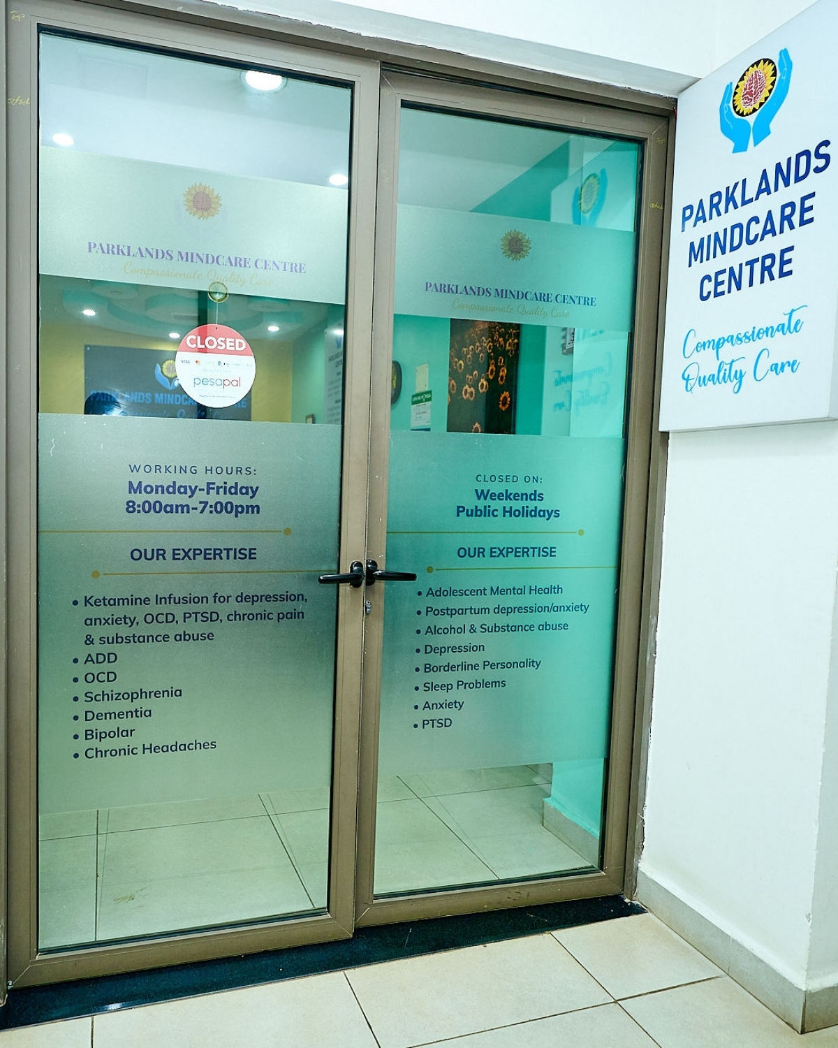 The etched-glass doors at the entrance to Parklands Mindcare Centre listing the conditions treated, including ketamine infusion, depression, anxiety, PTSD, OCD, bipolar, postpartum, adolescent mental health, and addiction